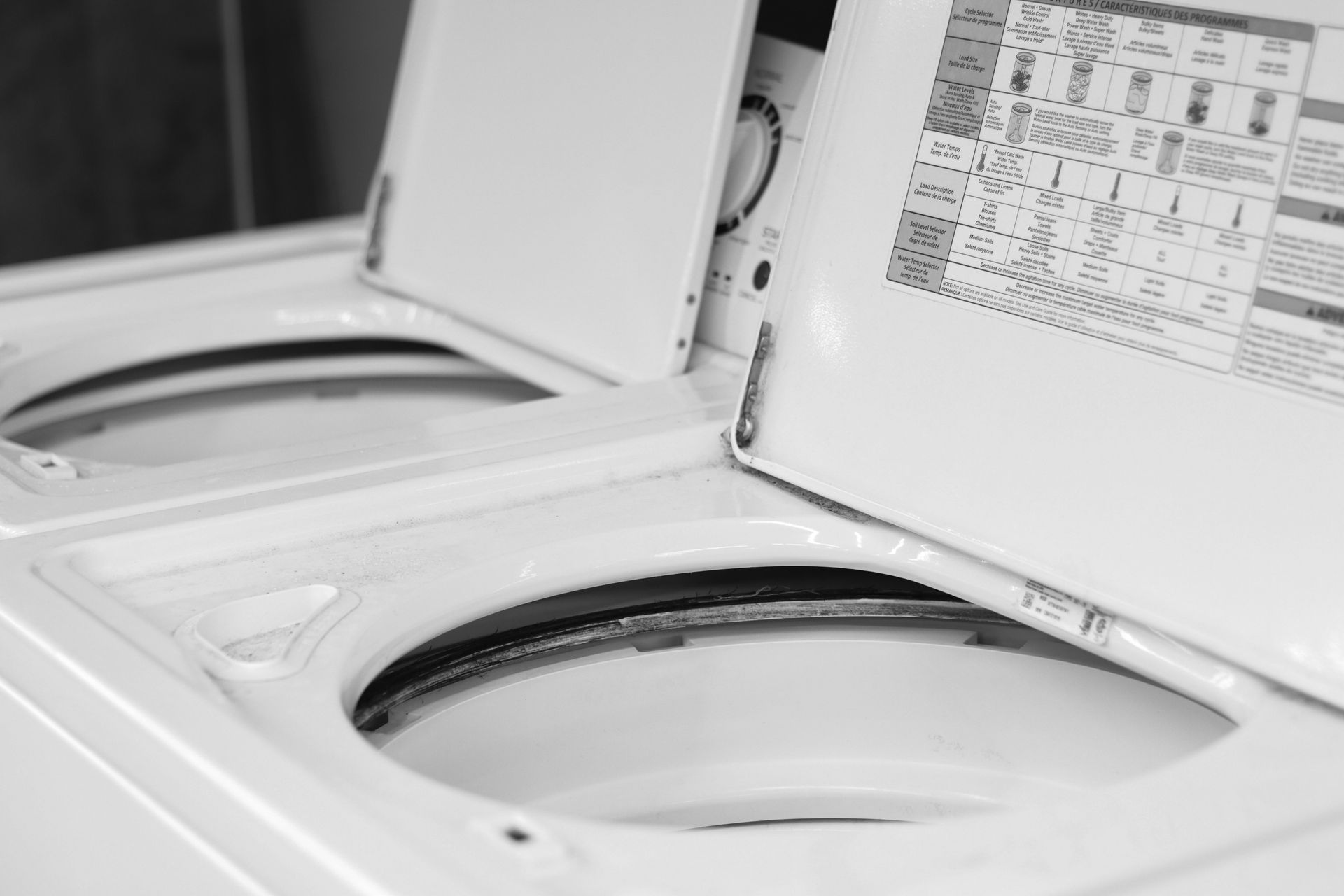 Two white washing machine tubs with open lids, indoors.