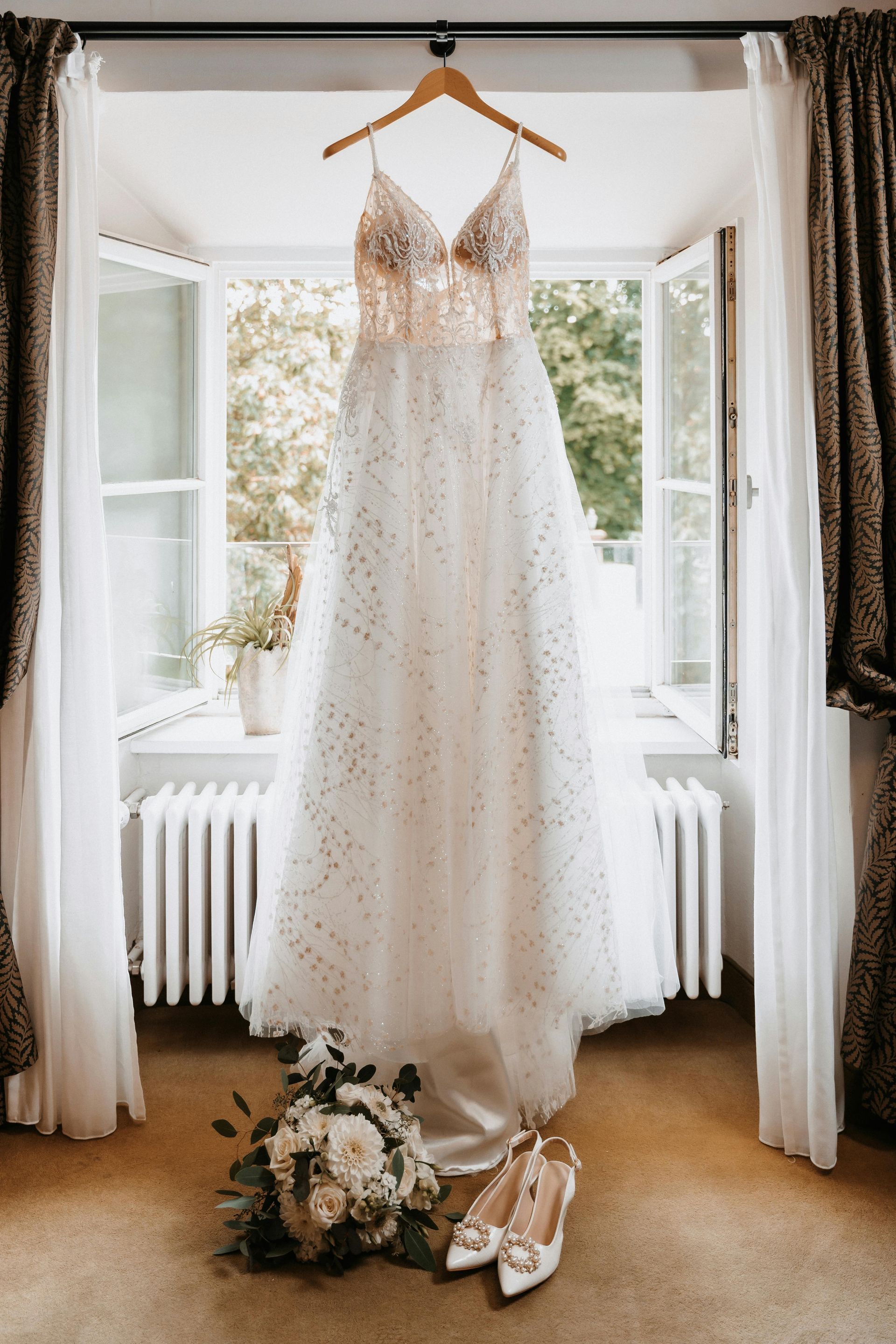 Wedding dress on a mannequin in front of a window with beige curtains.