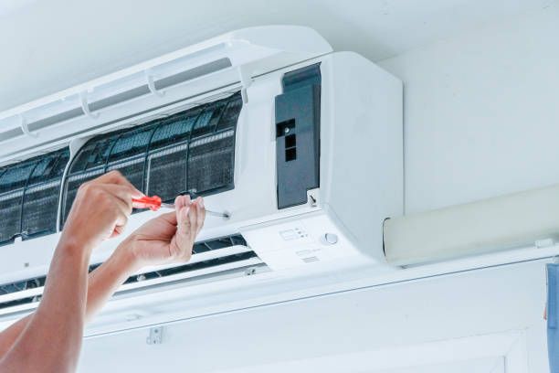 A person using a screwdriver to work on a wall-mounted air conditioning unit.
