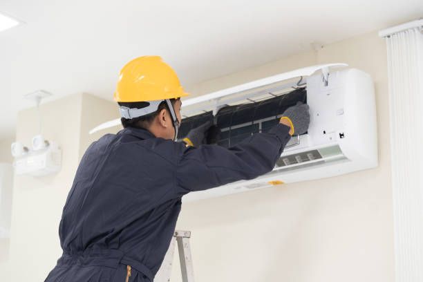 HVAC technician in yellow hard hat cleans air filter of a wall-mounted air conditioner.