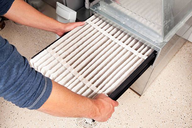 Person replacing an air filter in an HVAC system; white filter, metal ductwork.