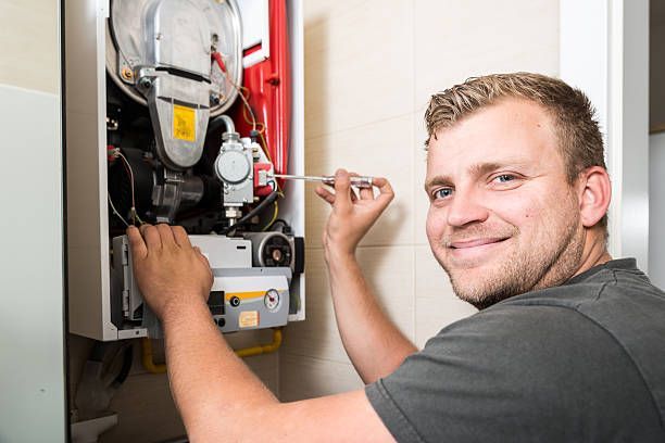 Man smiling while repairing a furnace with a screwdriver in a room.
