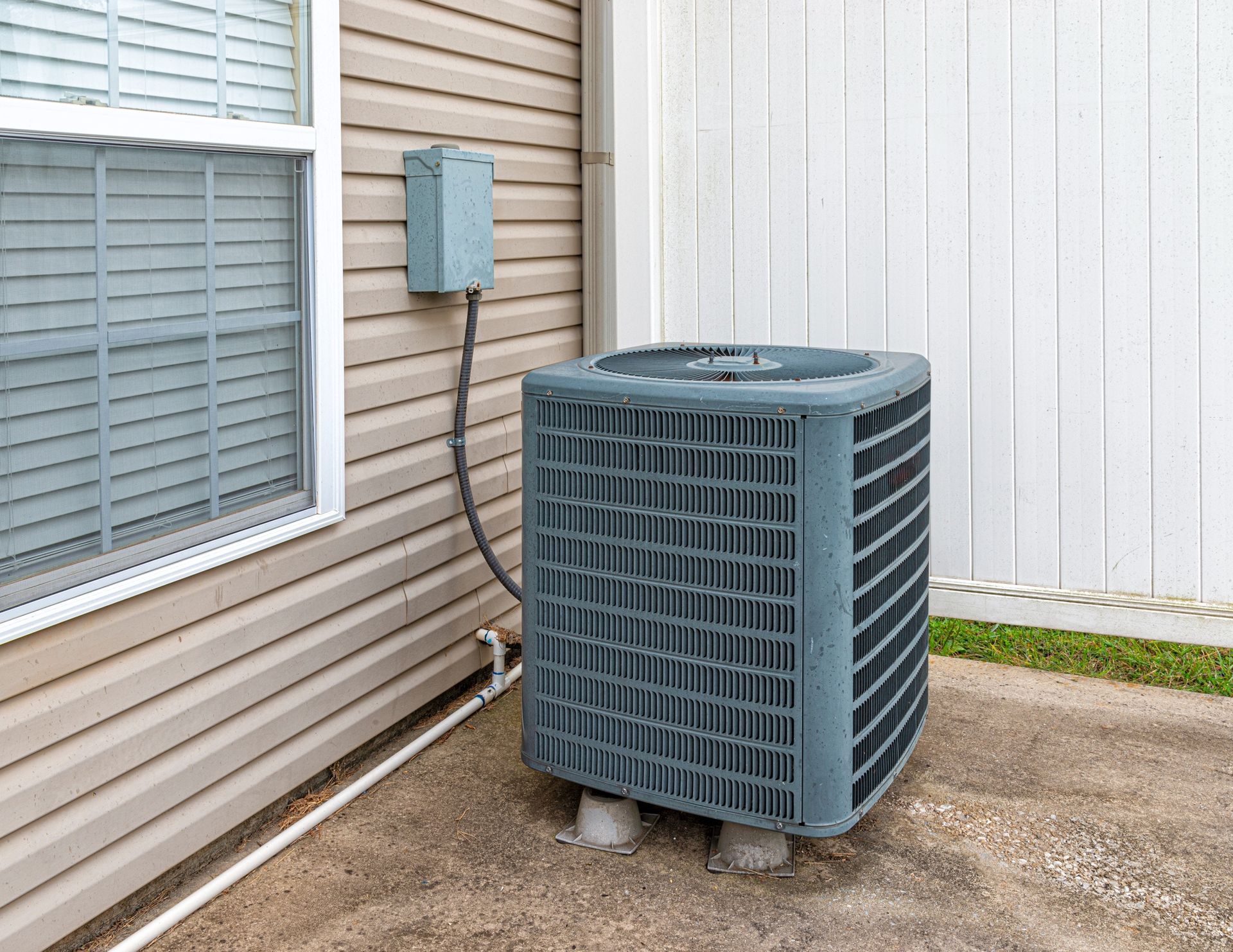 Air conditioning unit outside a building, near window and fence.