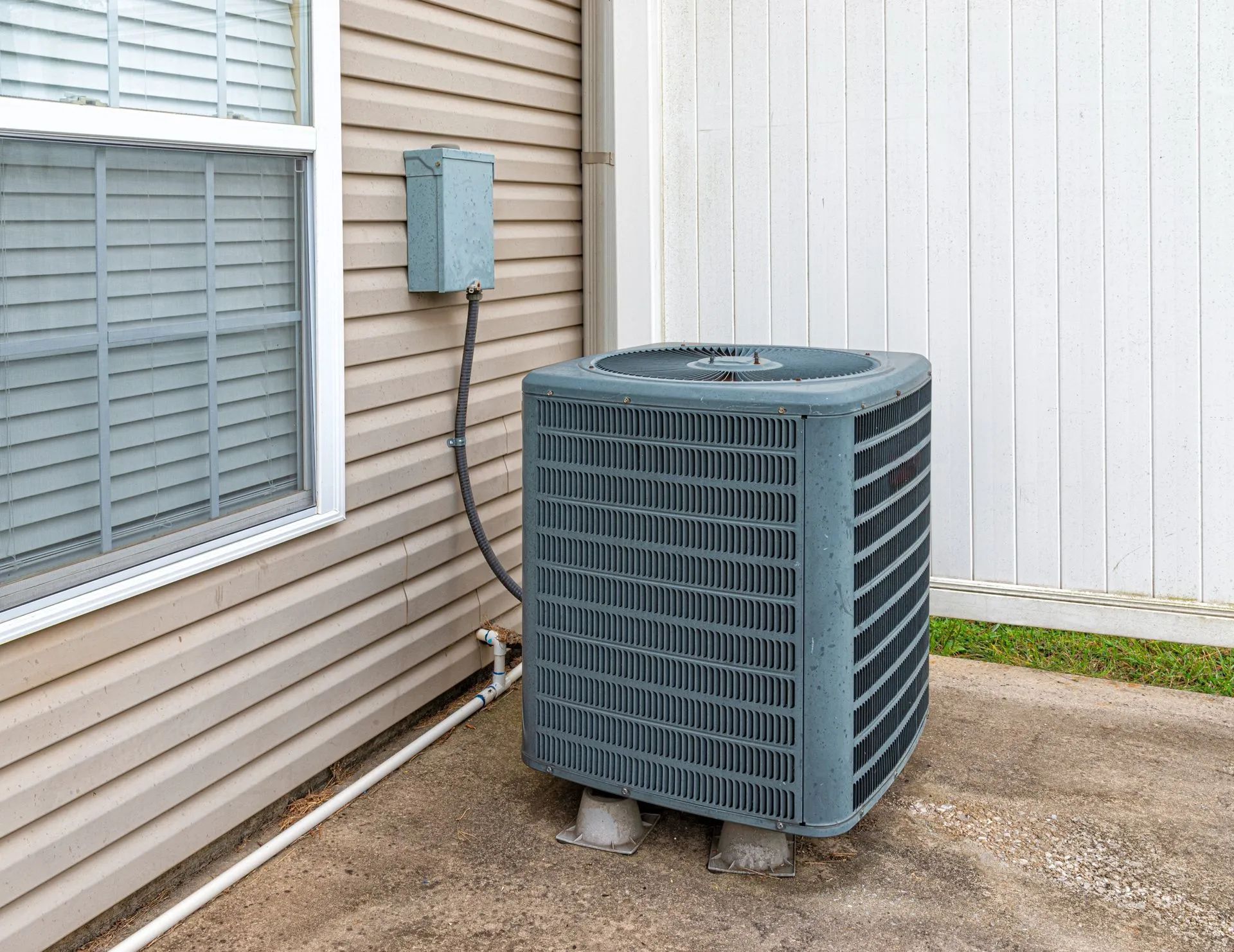 Outdoor air conditioning unit beside a beige house wall and window
