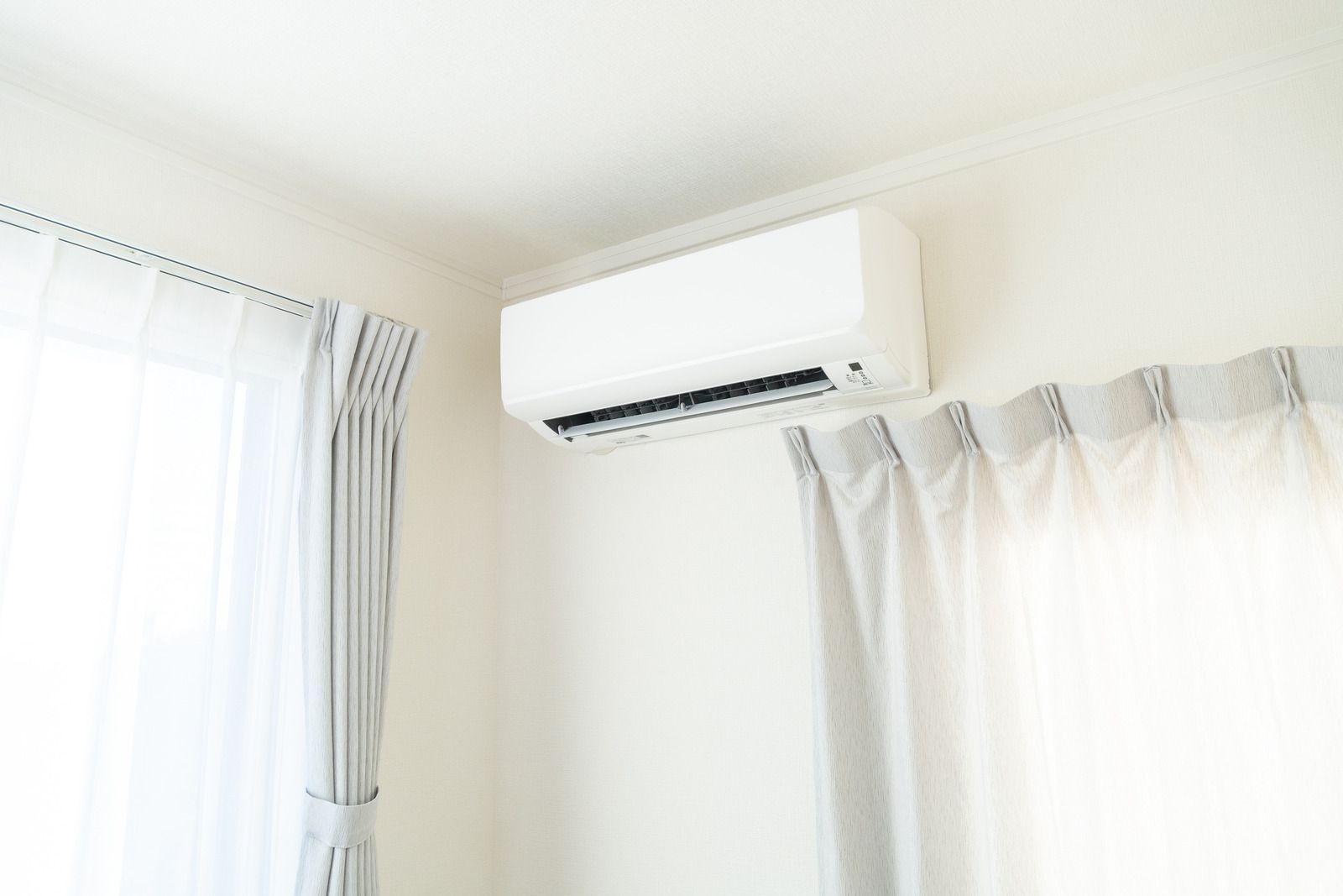 Bright room corner with a wall-mounted air conditioner above white curtains.