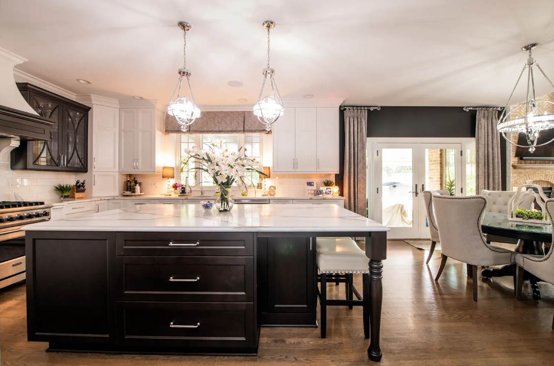 Modern kitchen with large island, dark cabinets, pendant lights, and dining area beside patio doors