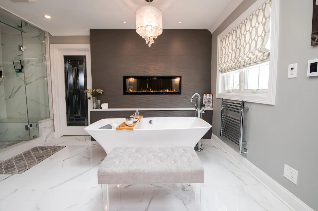 Modern white bathroom with freestanding tub, glass shower, dark accent wall, and window seat