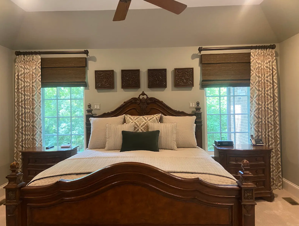 Elegant bedroom with a carved wooden bed, white bedding, dark curtains, and windows on both sides