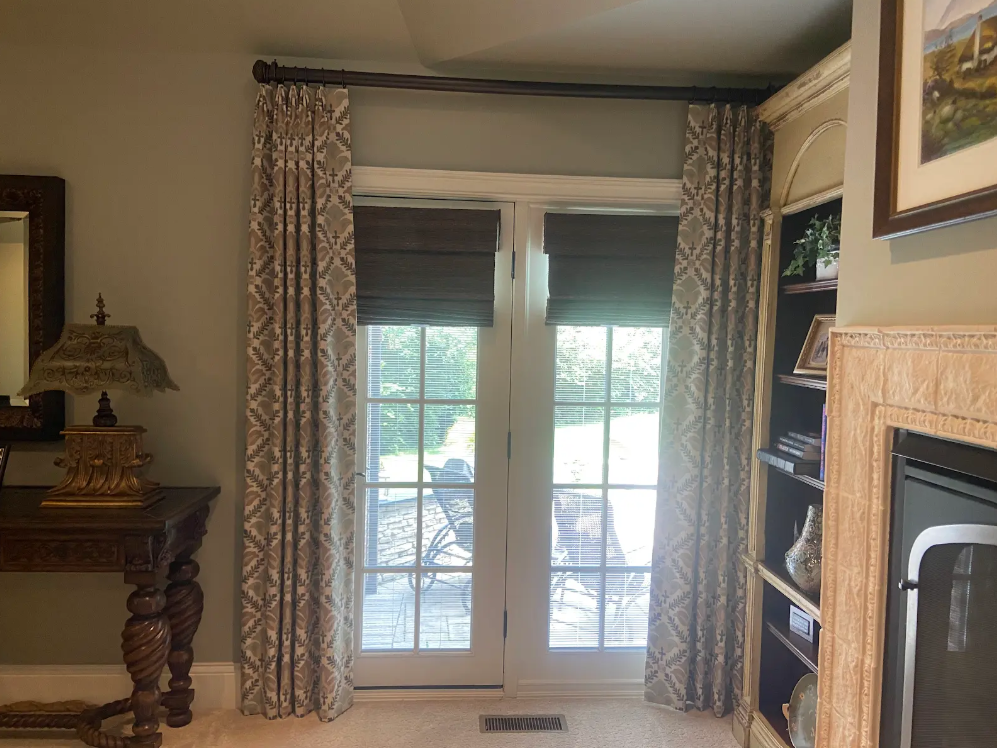 Living room with French doors, patterned curtains, wooden side table, and built-in shelves.