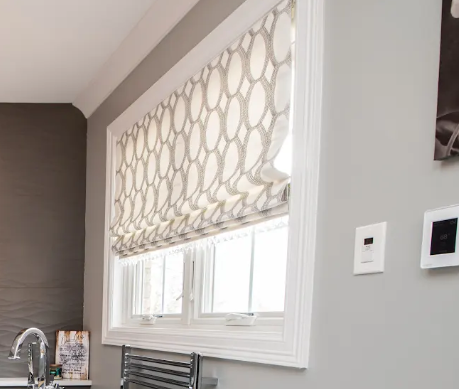 Bright kitchen window with patterned Roman shade, gray walls, and sink faucet below