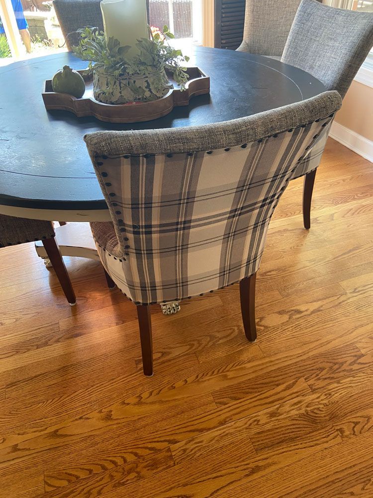 Dining room chair with plaid backrest beside a round dark table on a hardwood floor