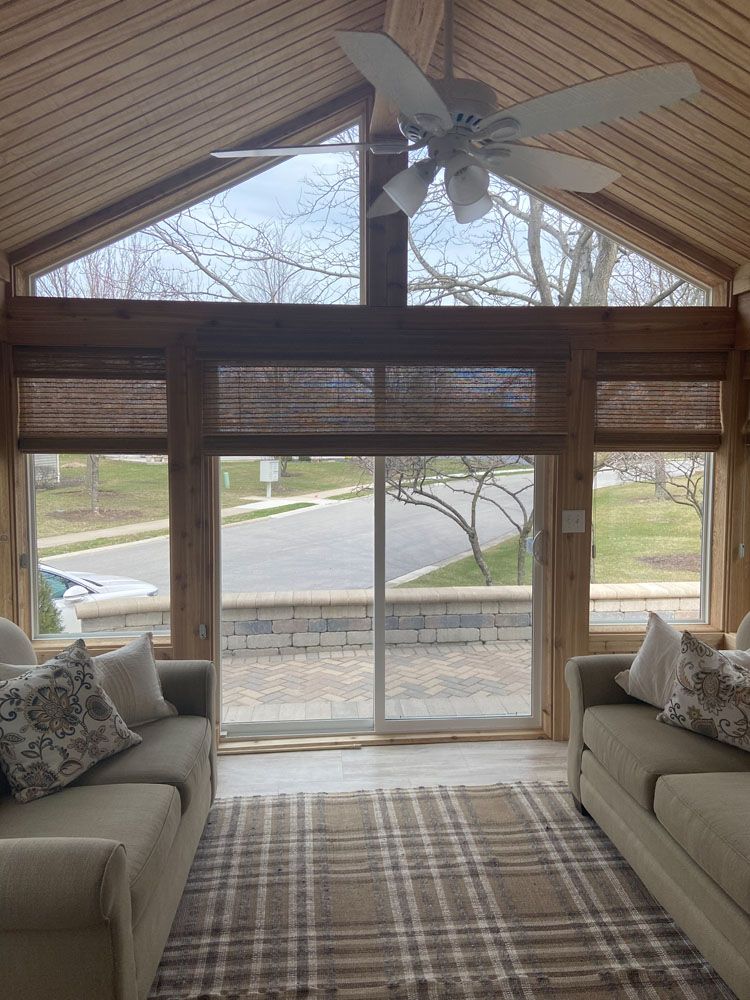 Bright sunroom with two beige sofas, large windows, and a view of a quiet street outside.