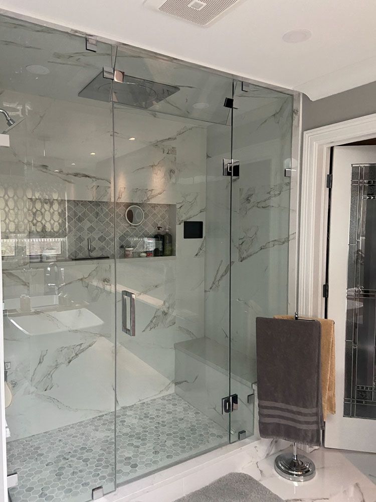 Glass walk-in shower with marble tiles, bench, and chrome fixtures in a modern bathroom