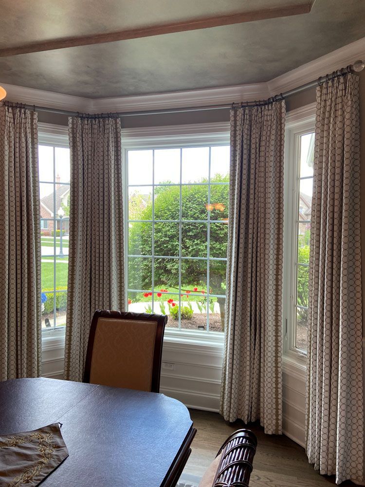 Dining room with bay window, cream curtains, and a view of a garden outside