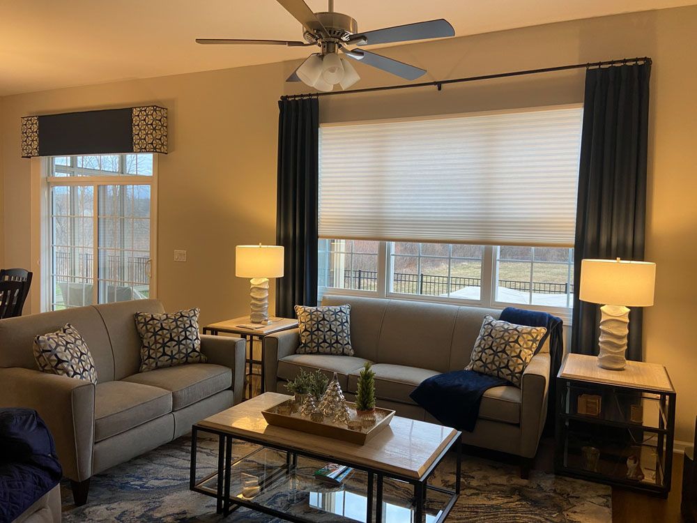Bright living room with two sofas, coffee table, lamps, ceiling fan, and large window with blinds and curtains