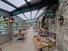 Terrasse extérieure de restaurant avec tables, chaises et muret en pierre sous une verrière.