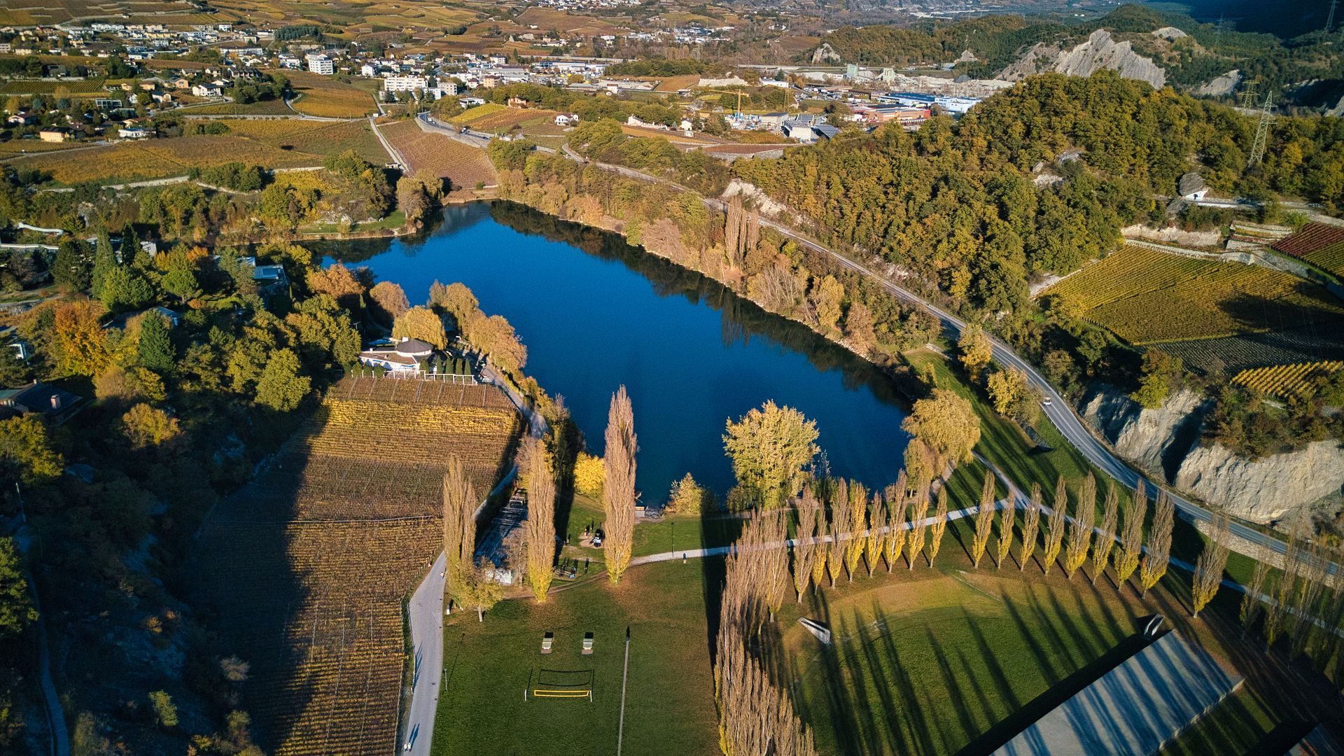 Vue aérienne d'un lac bleu entouré d'arbres, de murets de pierre et de champs dans un paysage rural
