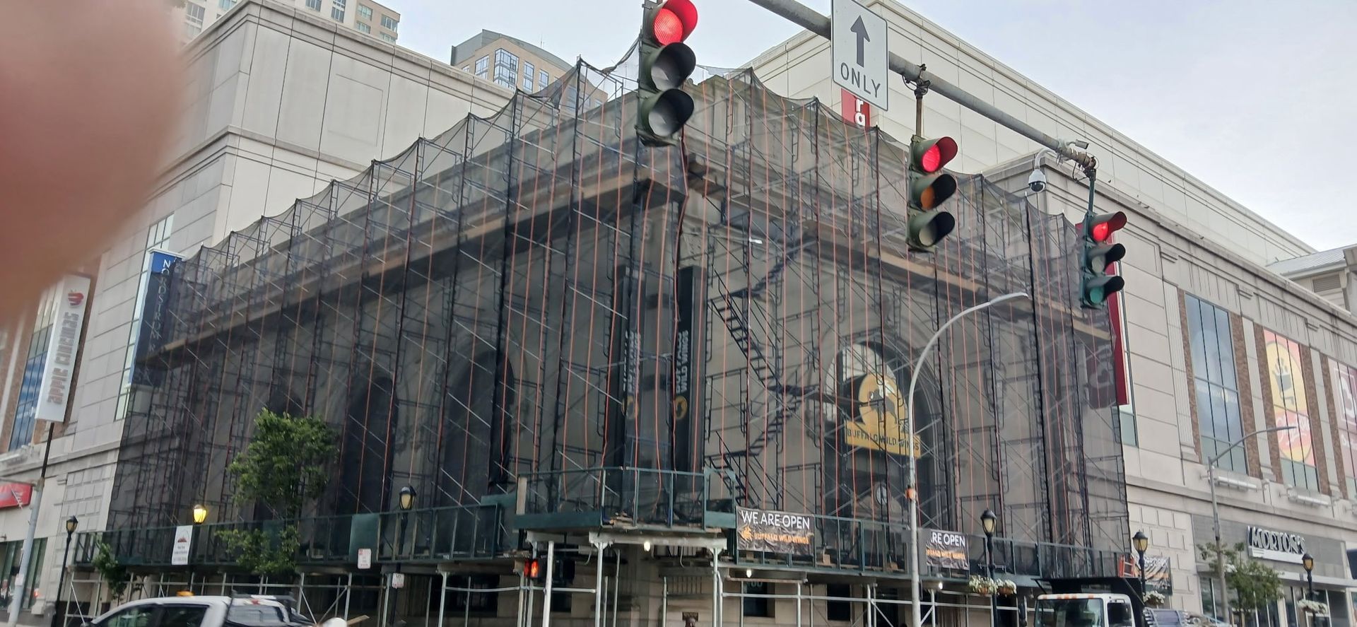 Building exterior under renovation, covered in scaffolding and netting, corner of street, traffic lights overhead.