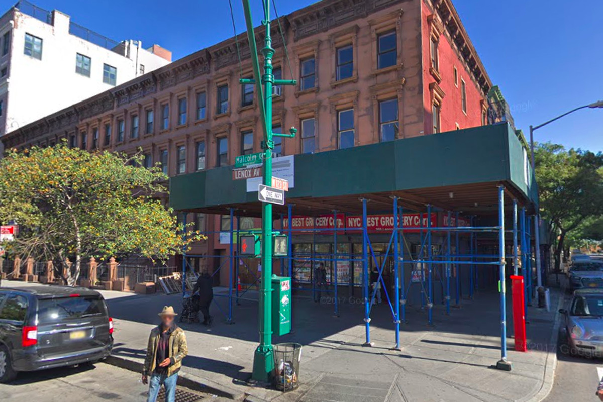Corner building with green scaffolding, a man standing in front of it, and parked cars.