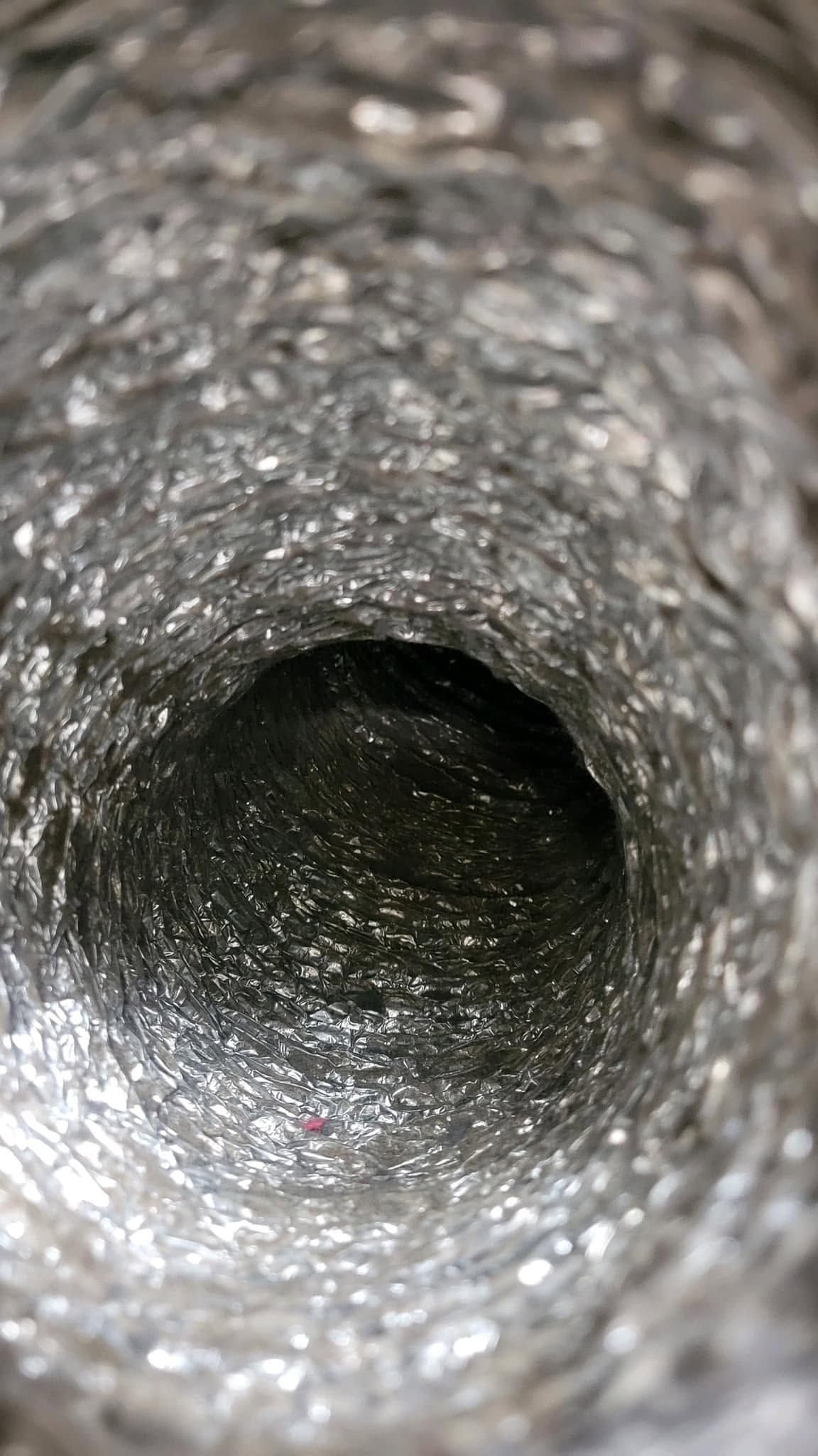 Close-up view down a metallic pipe interior with a dark circular opening at the center.
