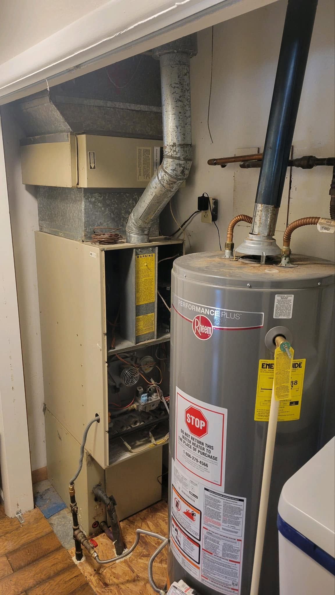 Water heater and HVAC furnace in a cramped utility closet with exposed ductwork and pipes.