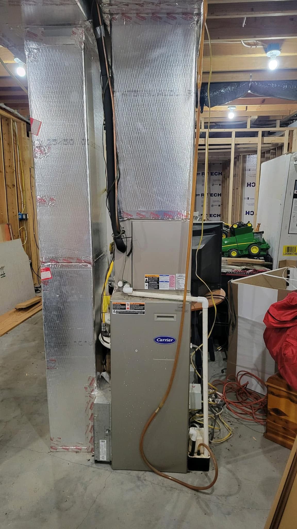 Basement utility area with large insulated ductwork and a furnace or HVAC unit beside storage shelves.