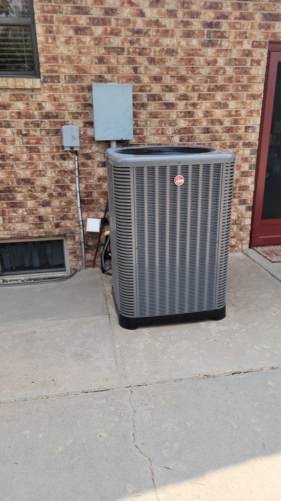 Outdoor air conditioner unit beside a brick wall and door on a concrete patio.
