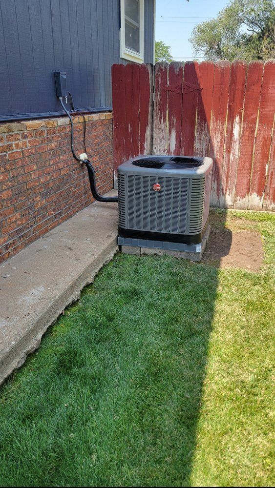 Backyard with a gray air conditioner unit beside a house and red fence, next to a grassy lawn.