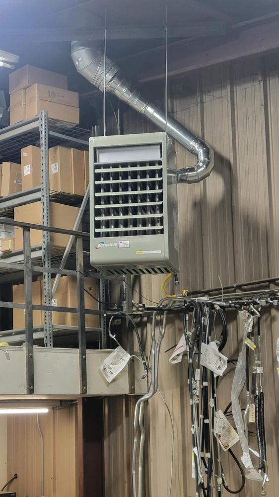 Industrial room with HVAC unit and ducting above shelves and hanging cables.