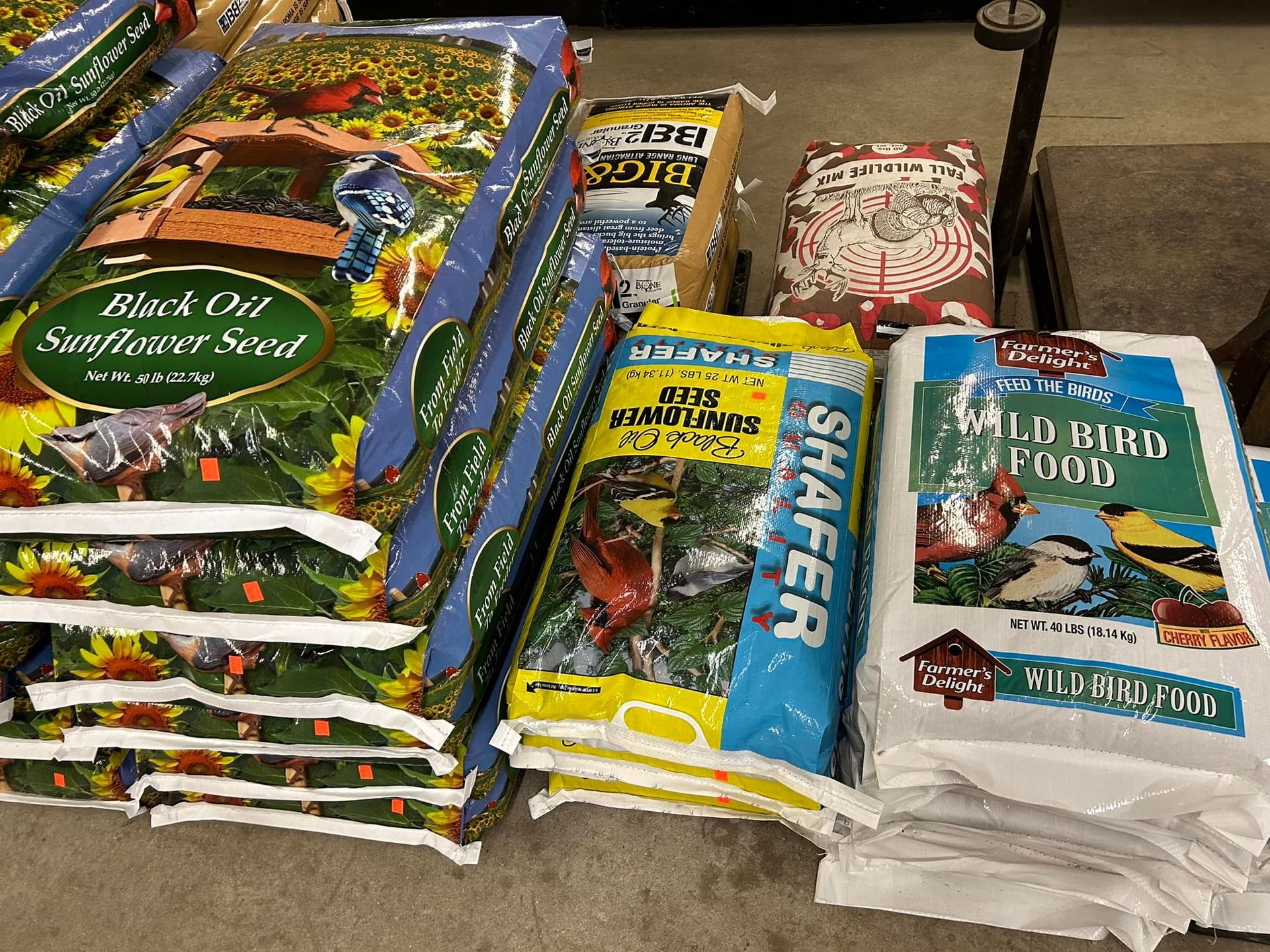 Stacked bags of birdseed for sale at a store, various brands and types including sunflower and wild bird food.