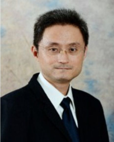 一名男子身穿深色西裝,繫著領帶,戴著眼鏡。他有著黑髮,面帶微笑。