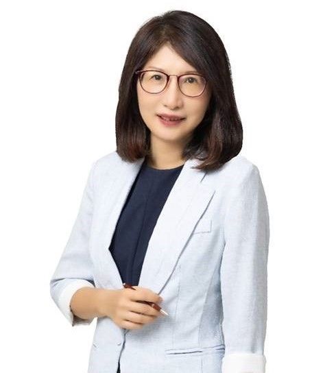 戴著眼鏡、身穿淺藍色西裝外套的女士微笑著,手裡拿著一支筆。