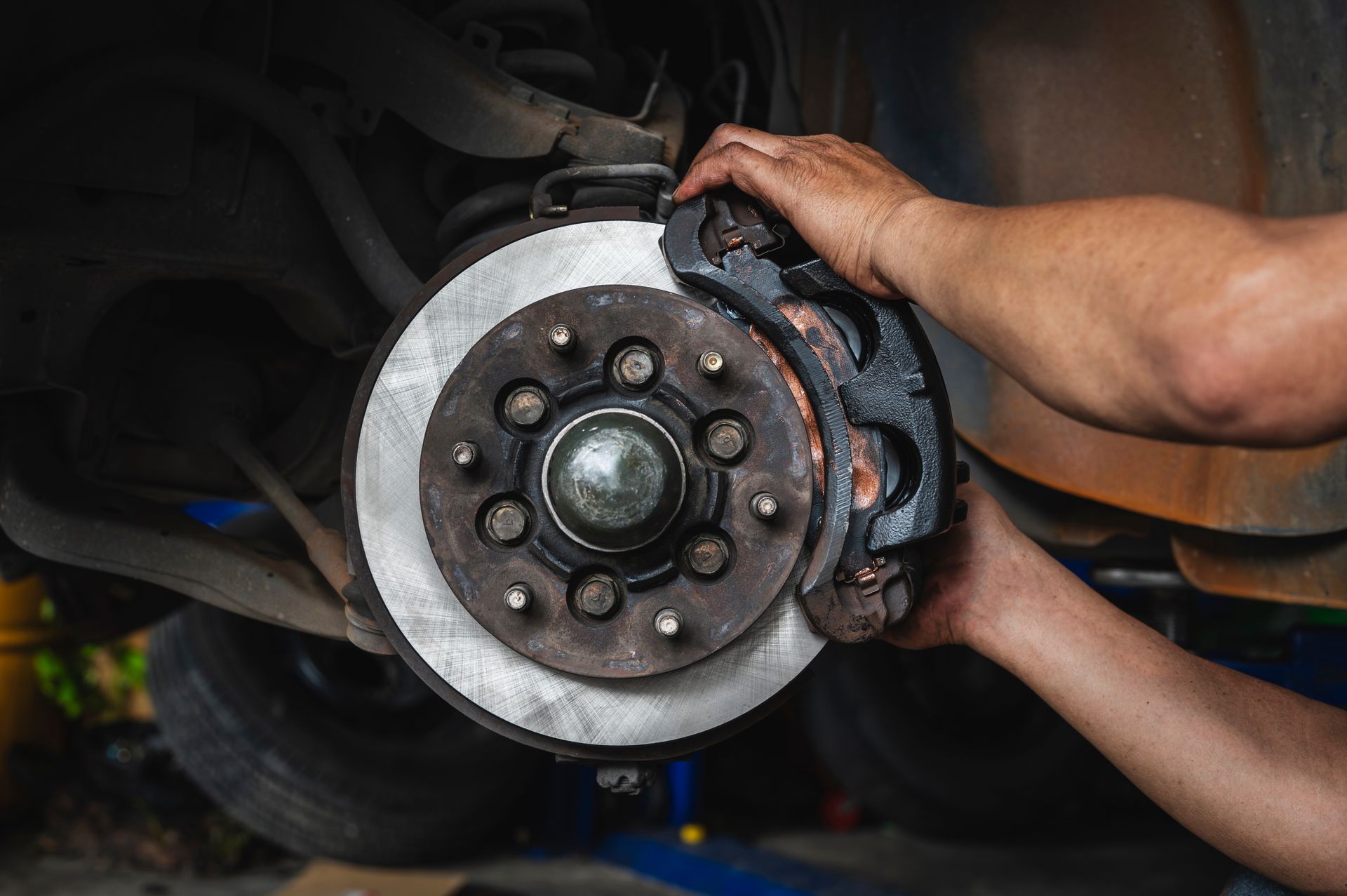 Hands holding a car brake rotor and caliper during auto repair in a garage.