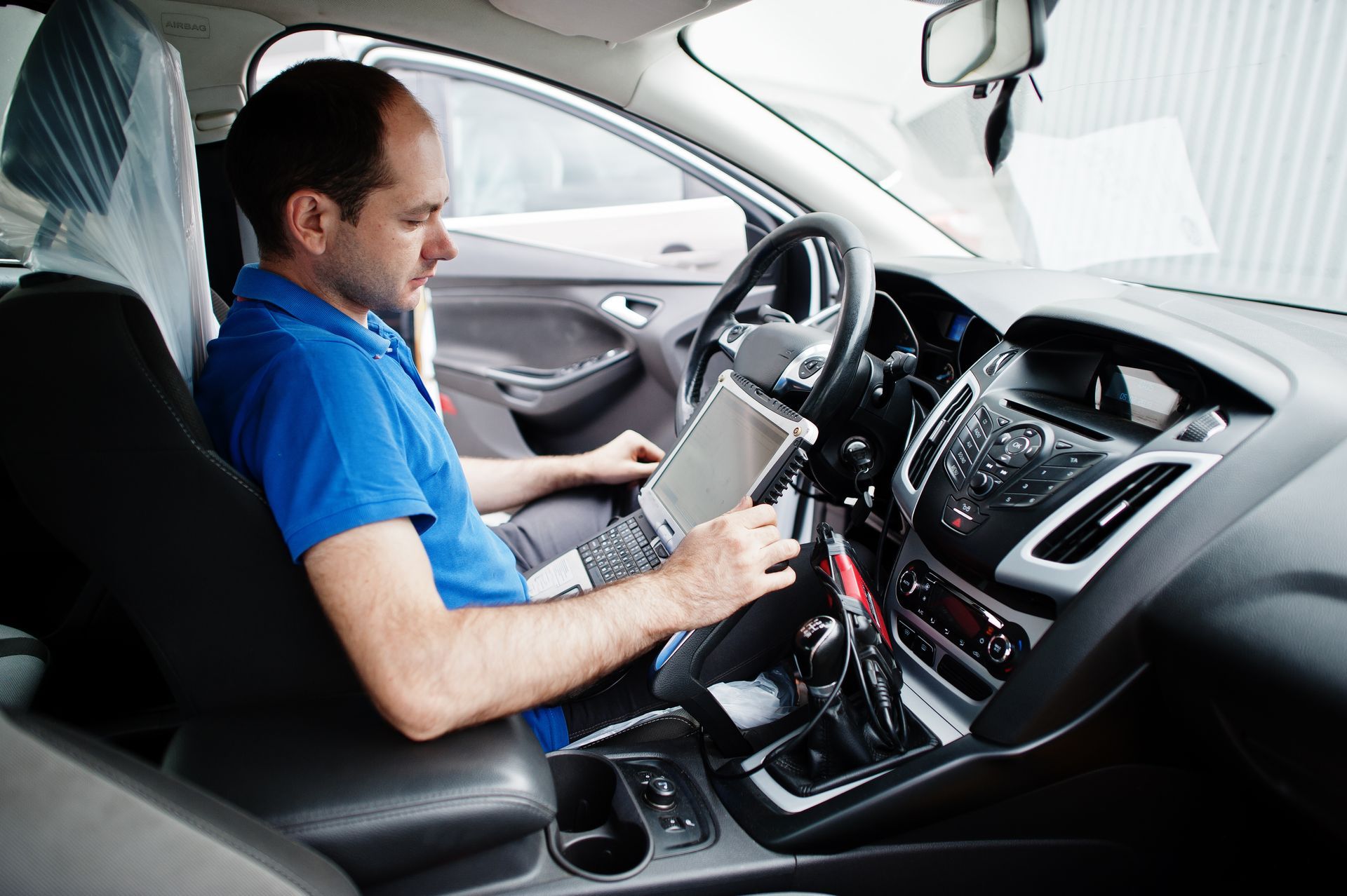 Man using a tablet inside a car; the device is connected to the car's system.