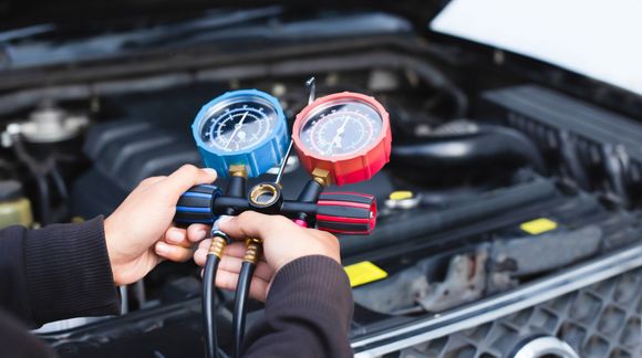 Person using gauges to check a car's air conditioning system in an engine bay.