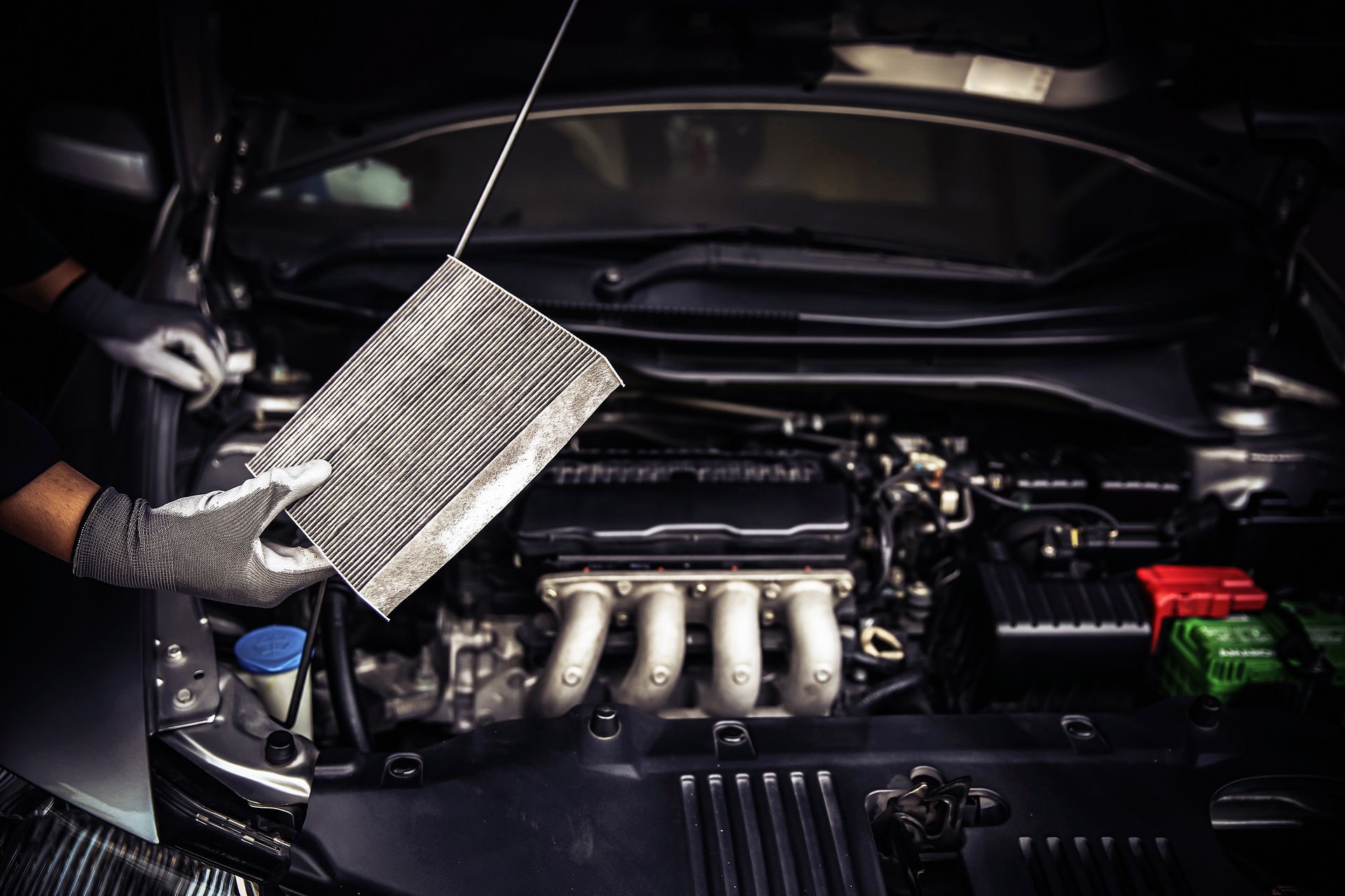 Person in gloves holding a dirty air filter near a car engine, inspecting it.