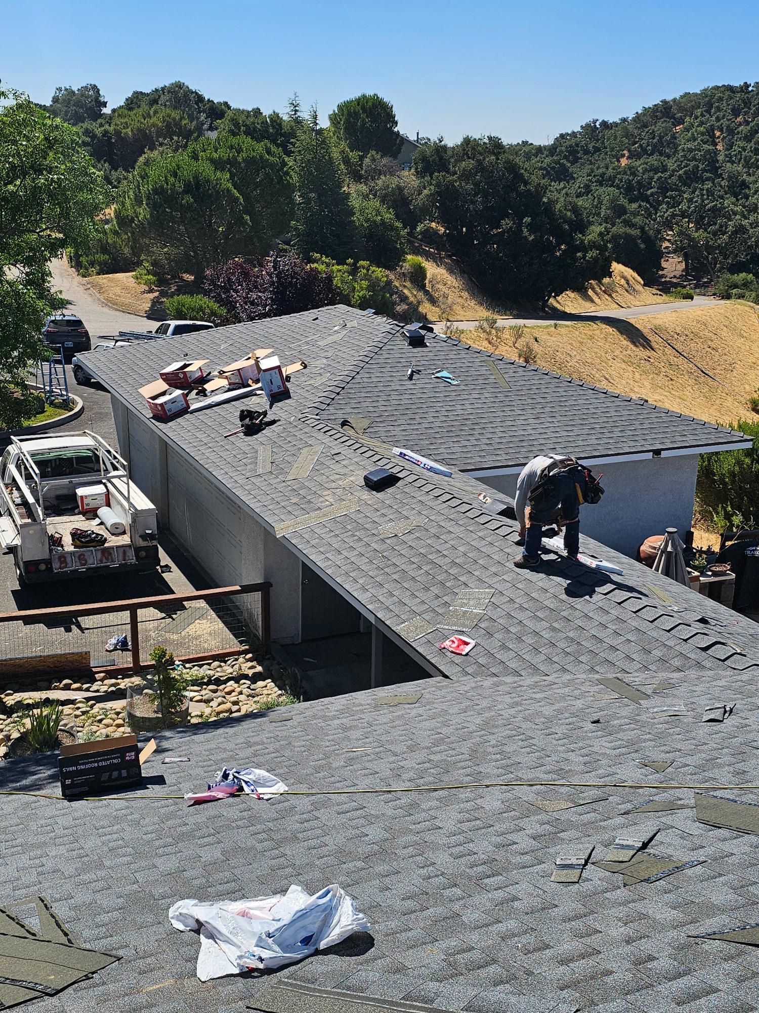 Roofers working on a gray shingle roof in a sunny hillside neighborhood
