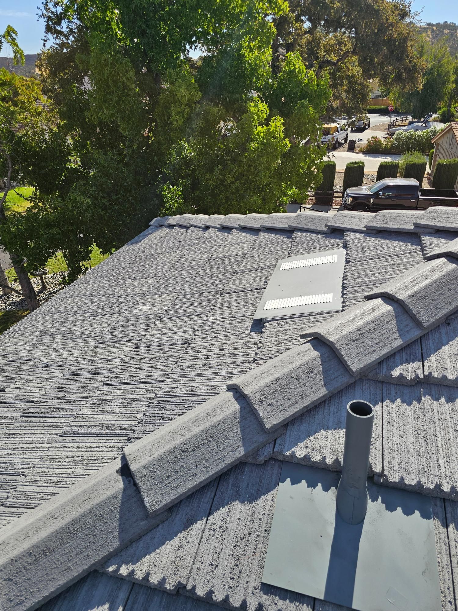 Gray shingled roof with skylight and vent, bordered by trees and parked cars below
