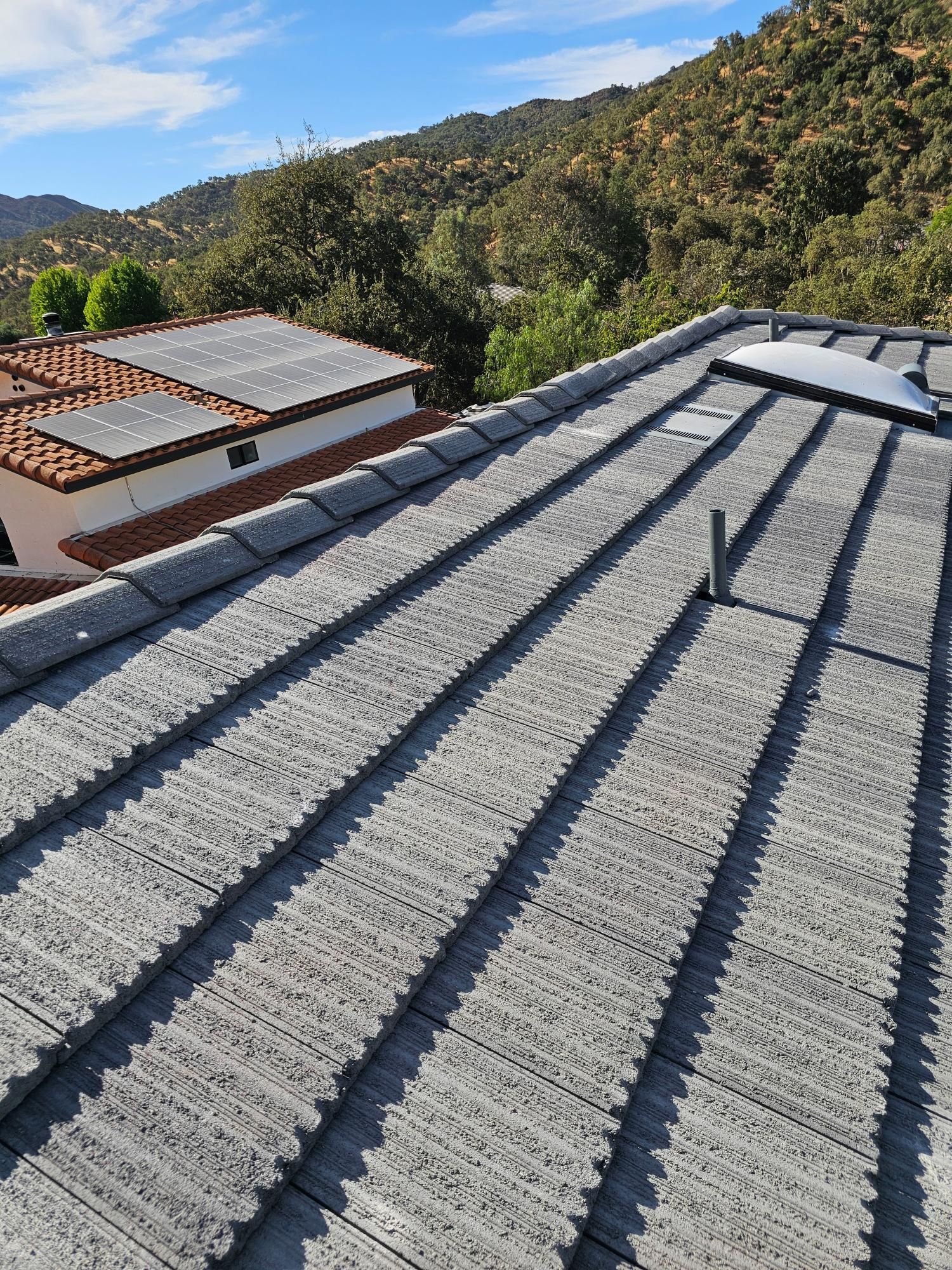 Rooftop with gray corrugated panels overlooking wooded hills and a building under a blue sky