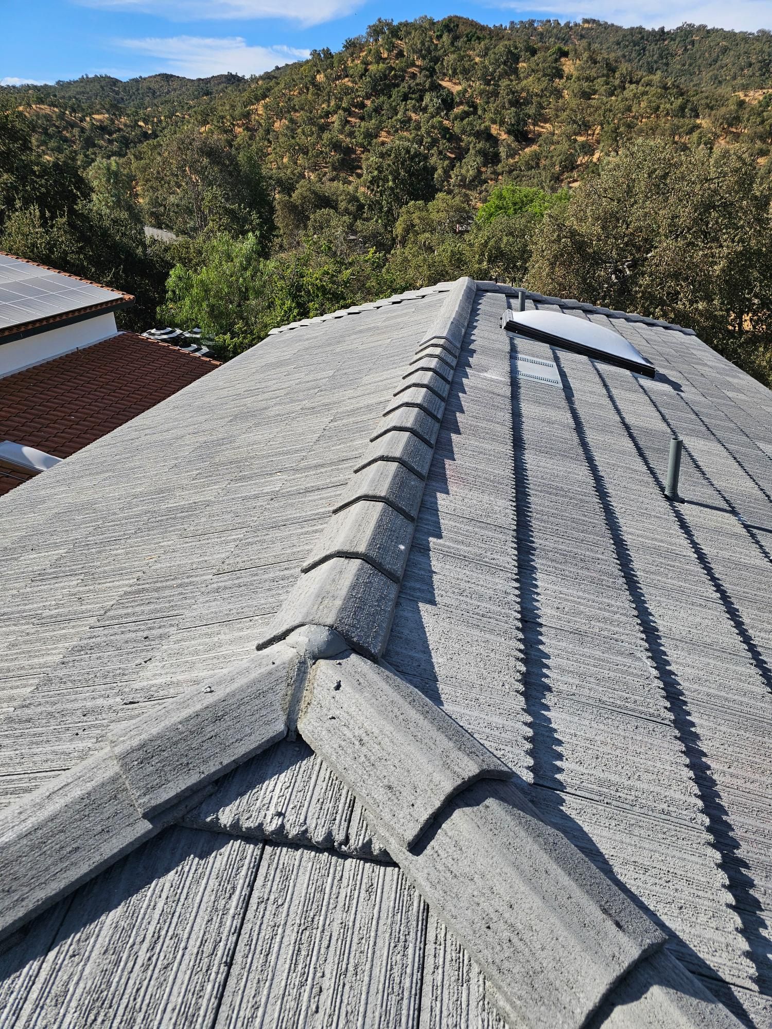 Roof with gray shingles and ridge cap, overlooking a wooded hillside under a clear blue sky