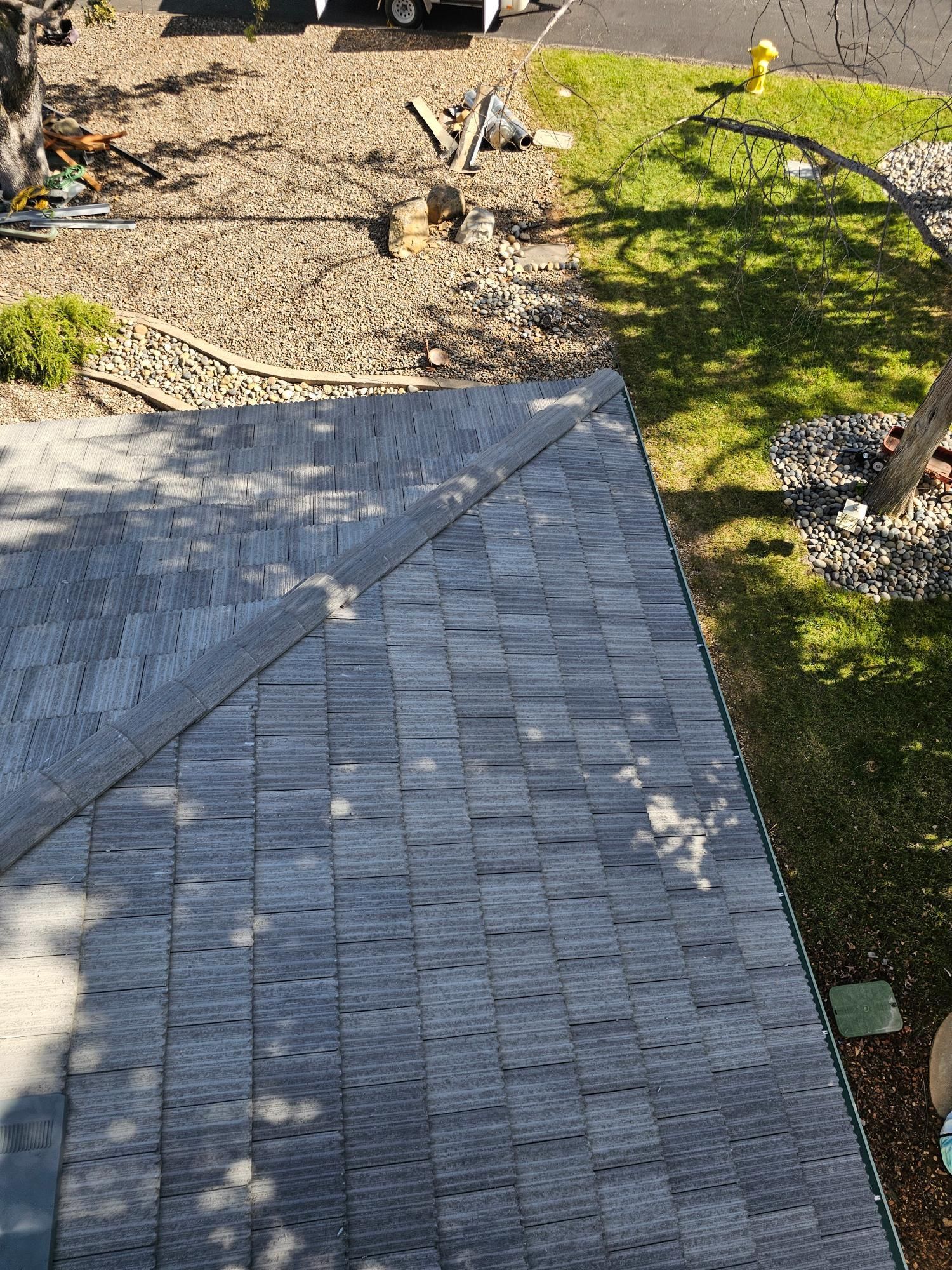 Paver walkway beside a gravel and grass yard with small shrubs and tree shadows