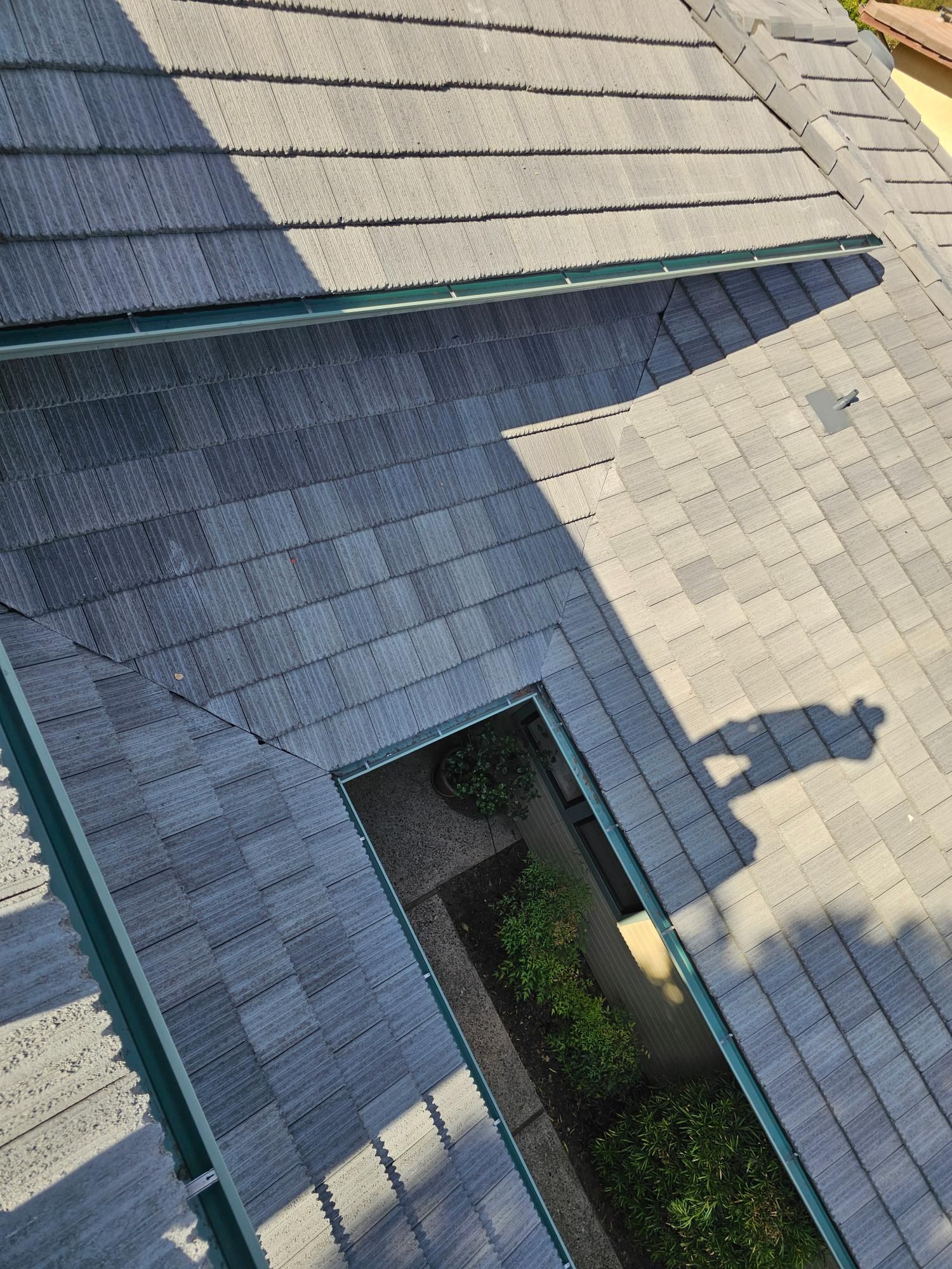 Aerial view of a gray-shingled roof with a skylight and a small garden beside it