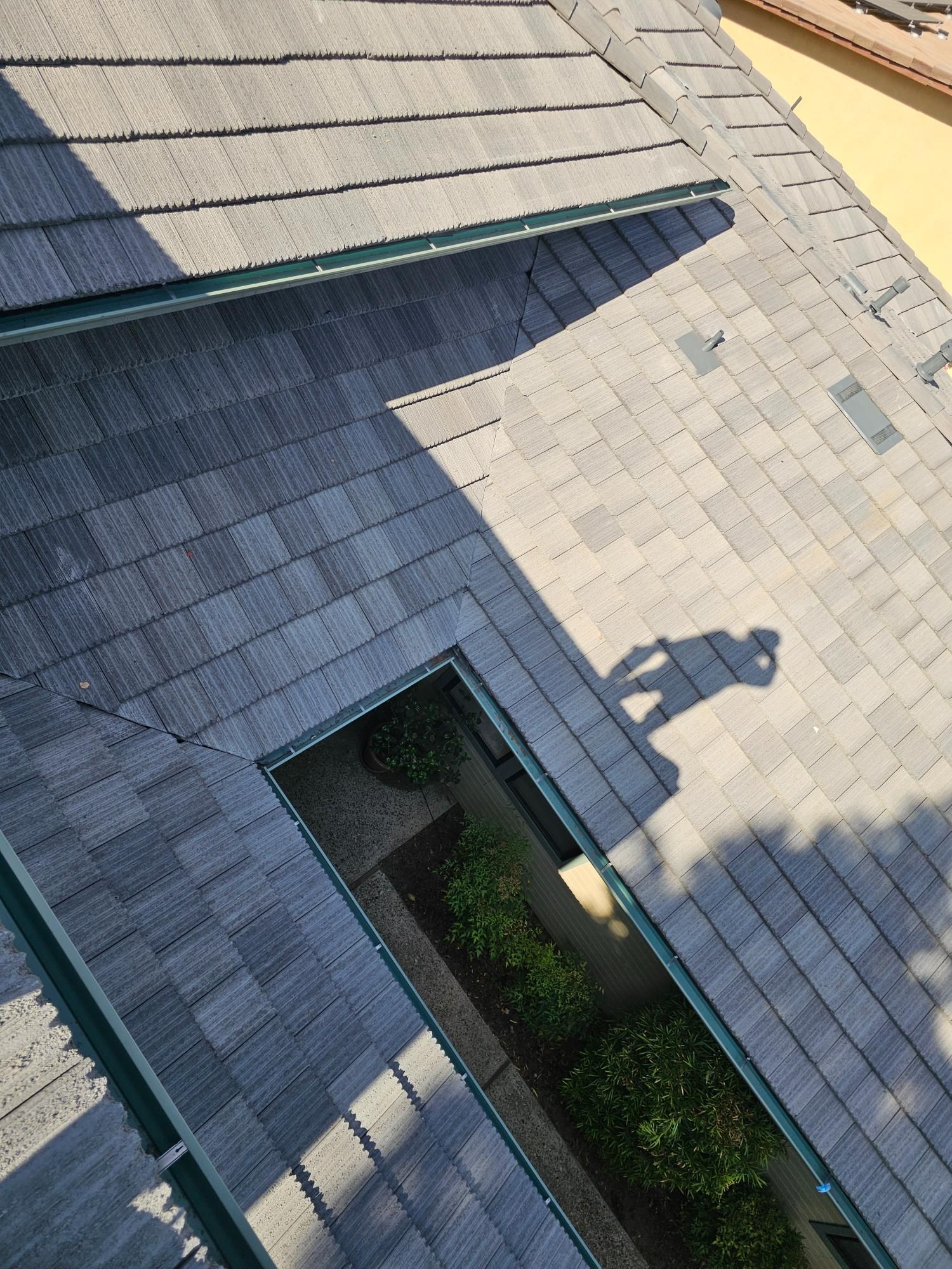 Aerial view of a gray shingled roof with a skylight and rooftop shadows.