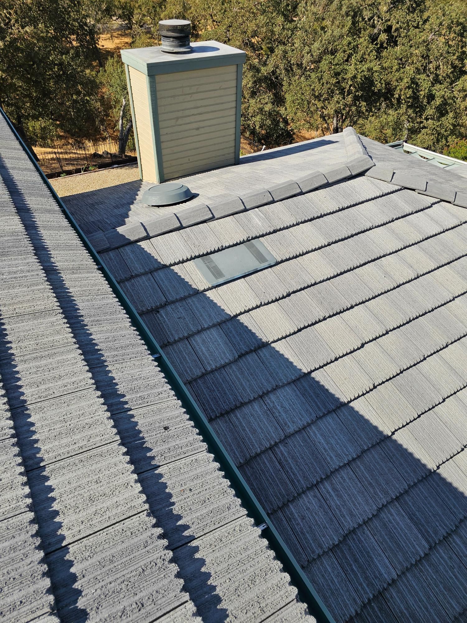 Residential roof with gray shingles and a small rooftop vent in sunlight