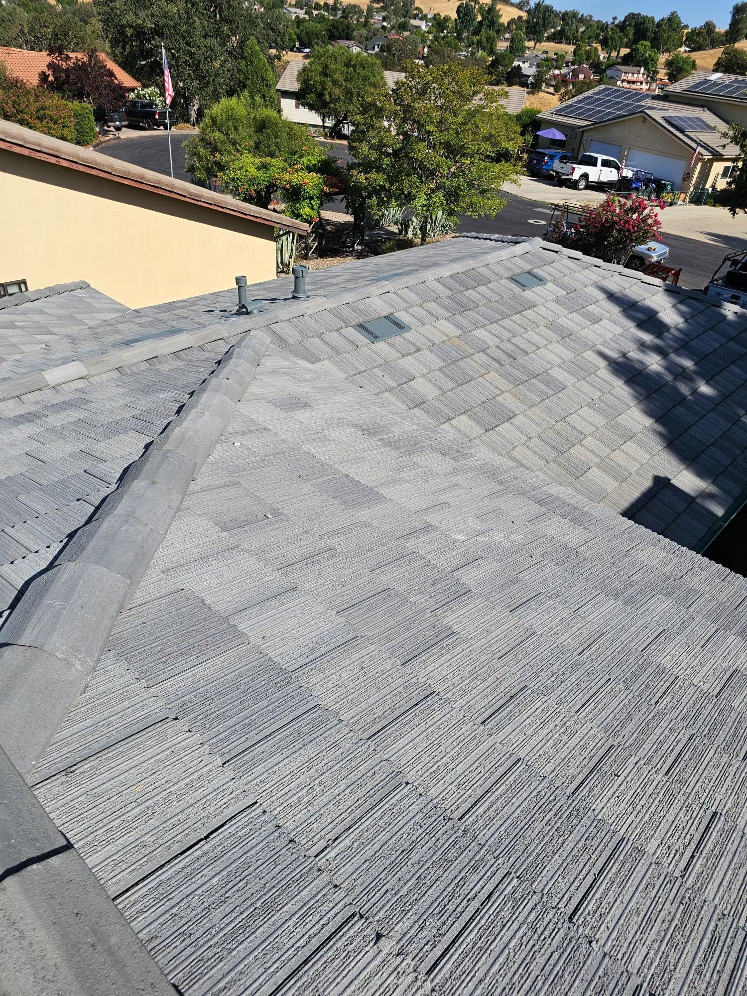 Roof shingles on a sloped rooftop overlooking a sunny residential neighborhood.