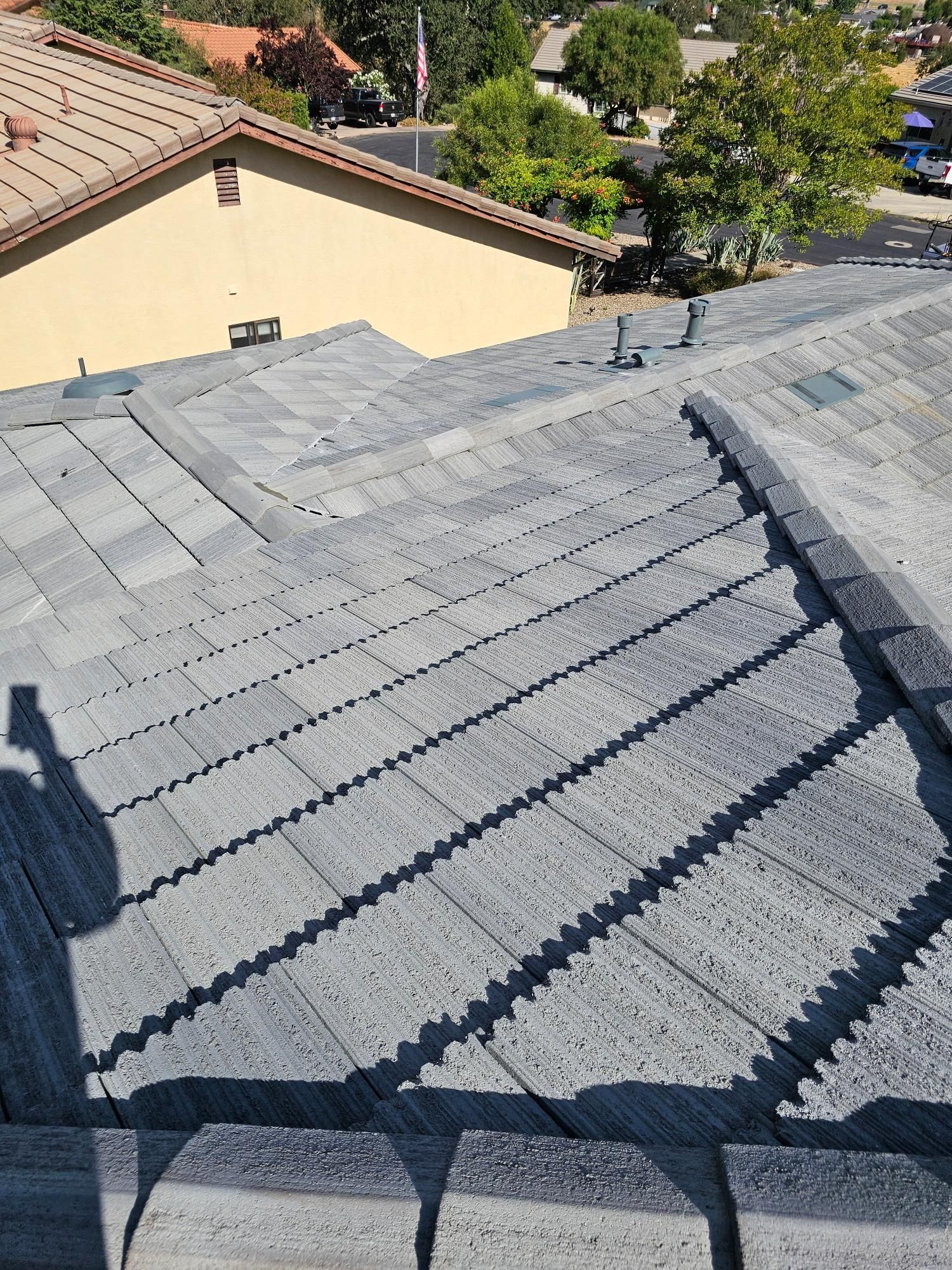 Gray shingled residential roof with sunlight and shadows, viewed from above near neighboring houses and trees