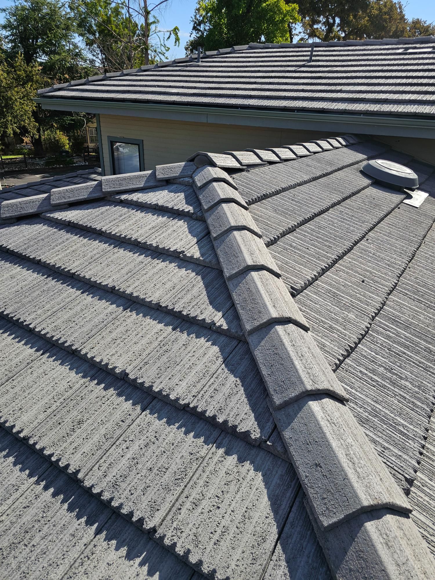 Gray shingle roof with a raised ridge line and rooftop vents under a clear blue sky