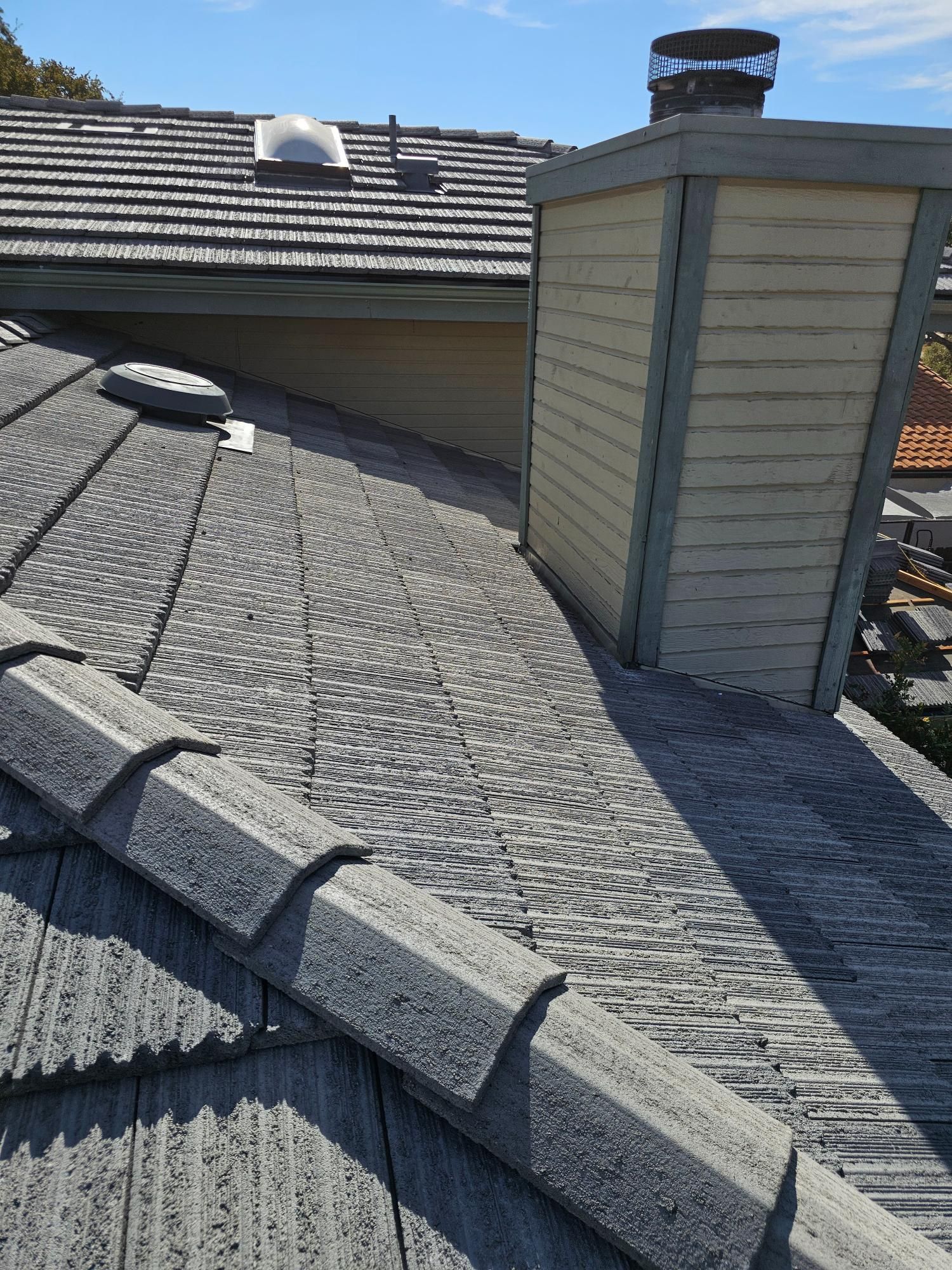 Gravel-covered rooftop with skylights, roof vents, and a chimney stack beside a sloped roof section