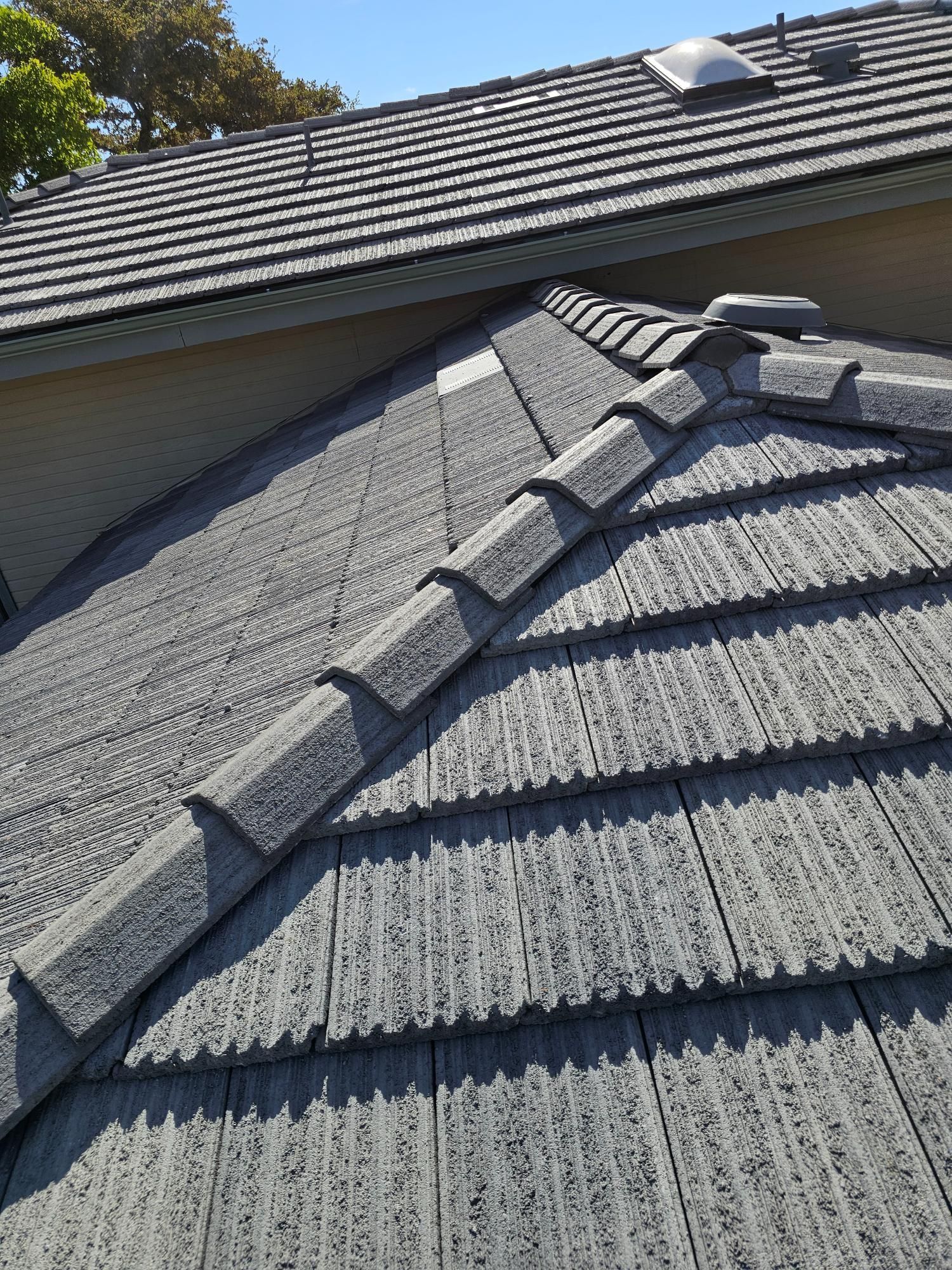 Gray tiled roof with a repaired ridge line on a house under clear sky