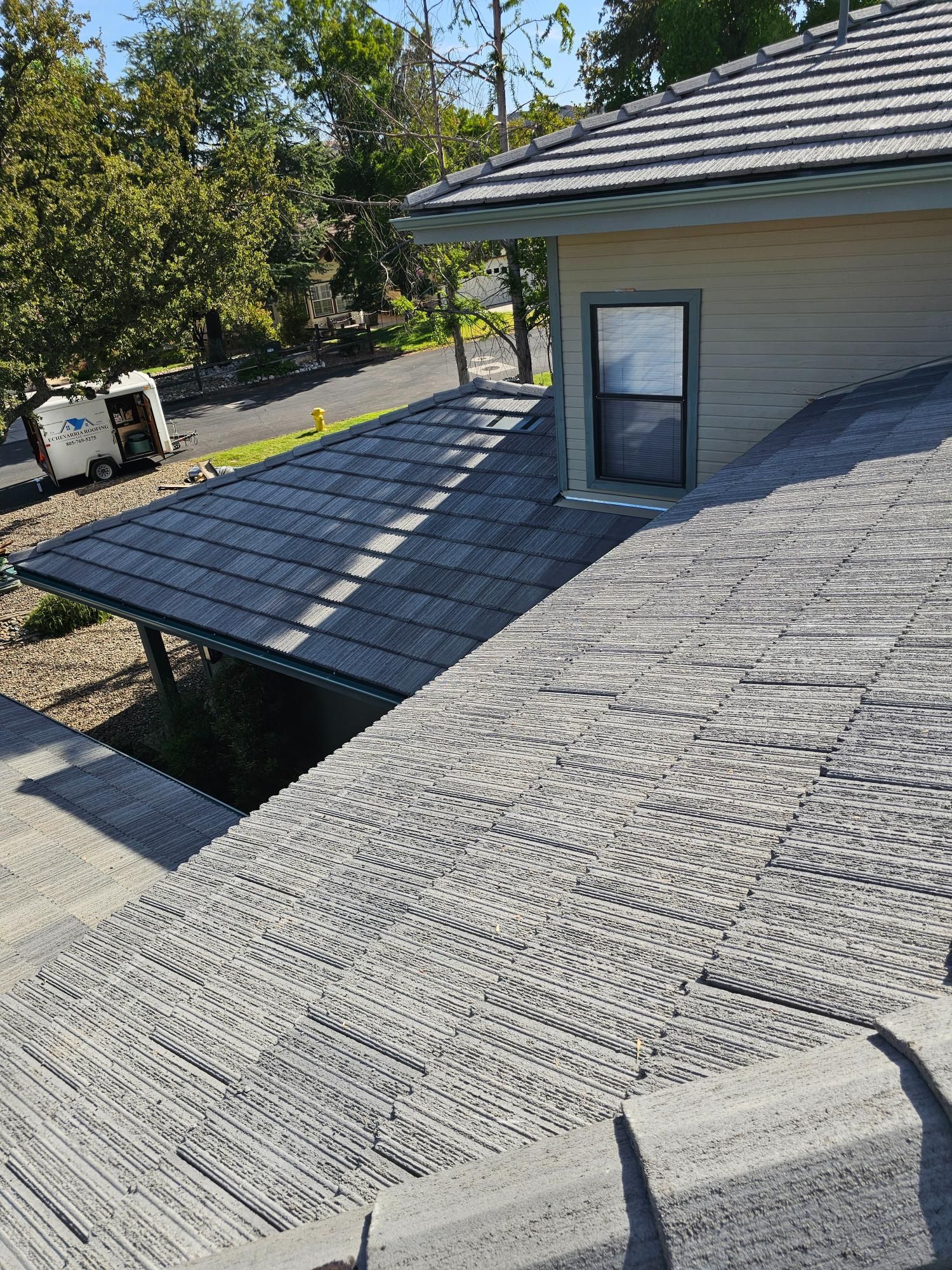 Roof with dark shingles and a dormer window beside a covered patio, with trees in the background